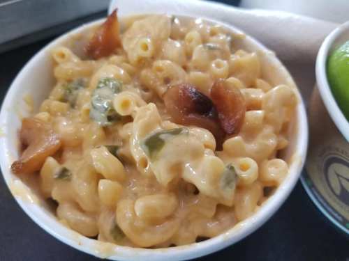 Creamy macaroni and cheese with green peppers and caramelized onions in a white bowl.