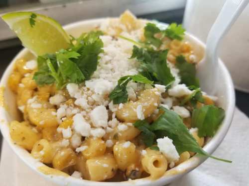 A bowl of creamy corn topped with cilantro, lime, and crumbled cheese.