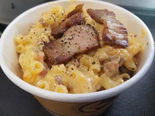 A bowl of creamy macaroni and cheese topped with crispy bacon pieces and black pepper.