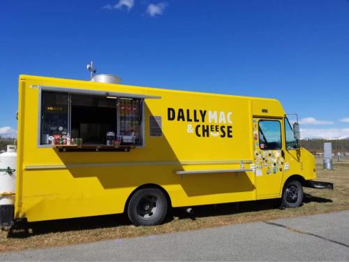A bright yellow food truck named "Dally Mac & Cheese" parked on a grassy area under a clear blue sky.
