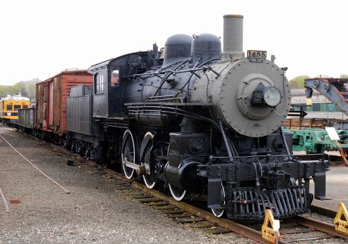 A vintage steam locomotive with a black exterior, parked alongside several freight cars on a railway track.