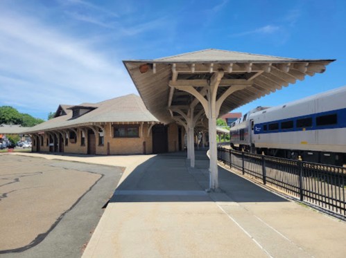 A train station with a covered platform and a train parked nearby, under a clear blue sky.