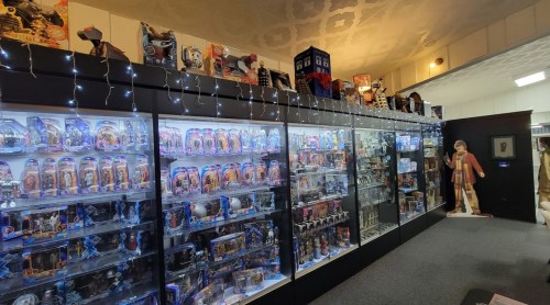 A display of collectible action figures and memorabilia in glass cases, with twinkling lights and a TARDIS model on top.