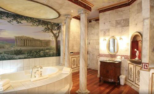 Luxurious bathroom with marble columns, a large tub, and a mural of ancient architecture on the wall. Elegant decor.