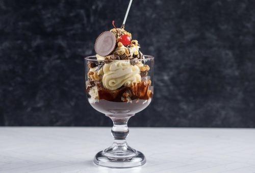 A decadent dessert in a glass, featuring layers of chocolate sauce, whipped cream, nuts, and a cherry on top.