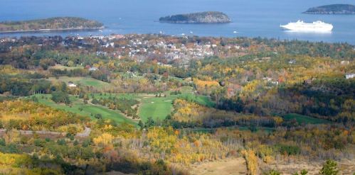 A scenic view of a coastal landscape with colorful autumn foliage, islands, and a cruise ship in the distance.