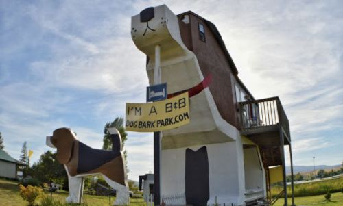 A large dog-shaped building with a sign reading "I'M A BOB" and a smaller dog statue in front, set against a blue sky.