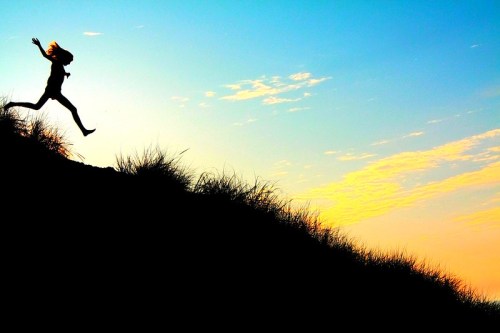 Silhouette of a person running on a hill against a colorful sunset sky with clouds.