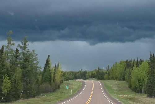 A winding road stretches through a forest under a dark, cloudy sky, hinting at an approaching storm.