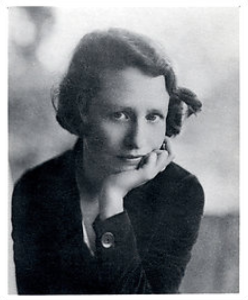 A black and white portrait of a woman with short hair, resting her chin on her hand, looking thoughtfully at the camera.