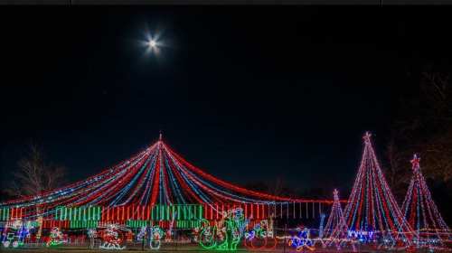 Colorful holiday lights illuminate a festive scene at night, featuring trees and decorations under a bright moon.