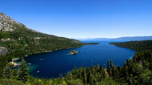 A scenic view of a blue lake surrounded by lush green trees and mountains under a clear blue sky.