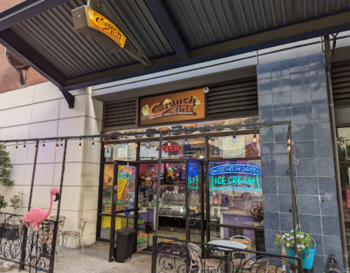 A colorful ice cream shop named "Crunch Time" with an open sign and outdoor seating, featuring a flamingo decoration.