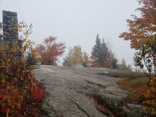 A foggy landscape with colorful autumn foliage and rocky terrain, featuring a stone structure in the background.