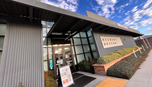 Exterior of the Hilbert Museum with a modern design, featuring large windows and a landscaped entrance.