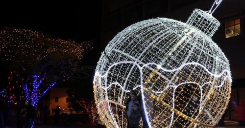 A large, illuminated ornament made of lights, surrounded by colorful holiday decorations at night.