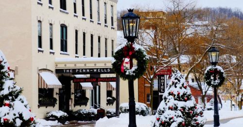 Snow-covered street scene featuring the Penn-Wells Restaurant, decorated with holiday wreaths and lampposts.