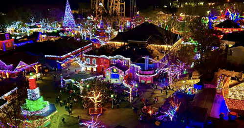 A vibrant holiday scene with colorful lights illuminating buildings and trees in a festive outdoor setting.
