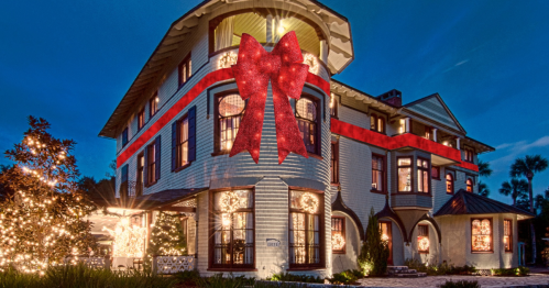 A beautifully decorated house with festive lights and a large red bow on the front, set against a twilight sky.
