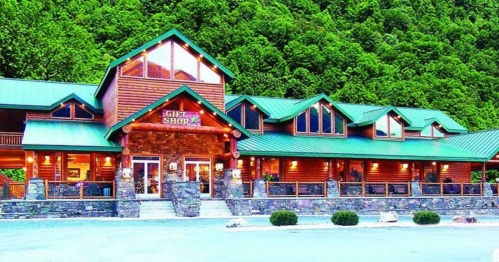 A large log cabin gift shop with a green metal roof, surrounded by lush green trees.