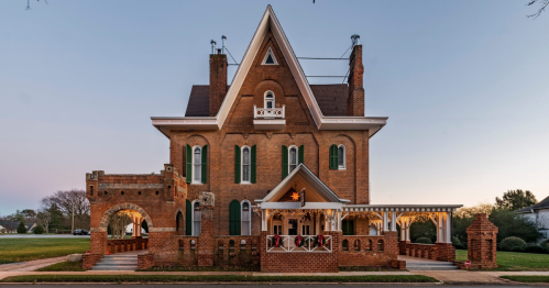A large, historic brick house with a unique architectural design, featuring a turret and decorative porch.