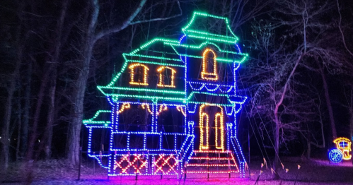 A brightly lit house decorated with colorful lights, surrounded by trees at night.