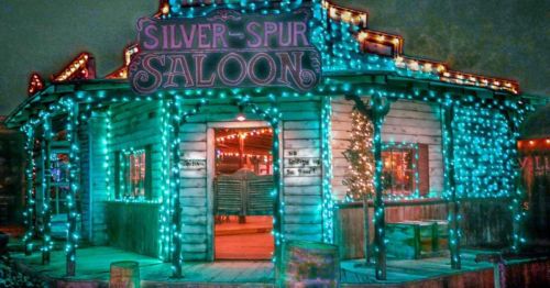 A brightly lit saloon with colorful lights, featuring a wooden exterior and a festive atmosphere.
