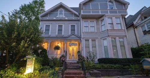 A charming Victorian-style house with a welcoming entrance, surrounded by greenery and flowers, at dusk.