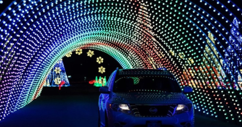 A car drives through a colorful light tunnel decorated with festive holiday lights and snowflake designs.