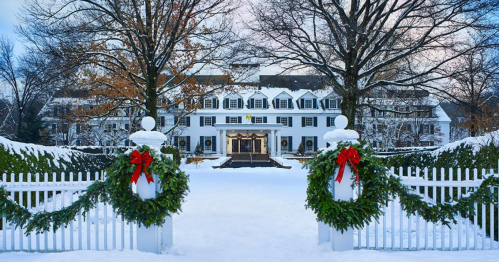 A snowy scene featuring a grand building framed by festive wreaths on a white picket fence.