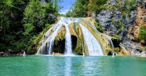A scenic waterfall cascading into a turquoise pool, surrounded by lush greenery and rocky cliffs.