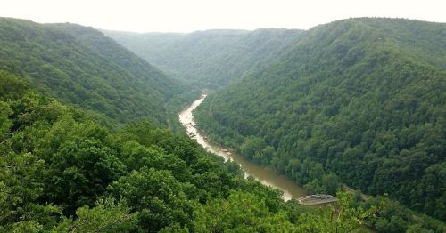 A scenic view of a winding river surrounded by lush green hills and valleys under a cloudy sky.