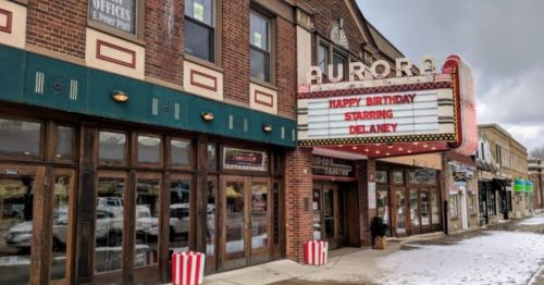 Exterior of the Aurora Theater with a marquee displaying "Happy Birthday Starring Delaney" and snow on the ground.