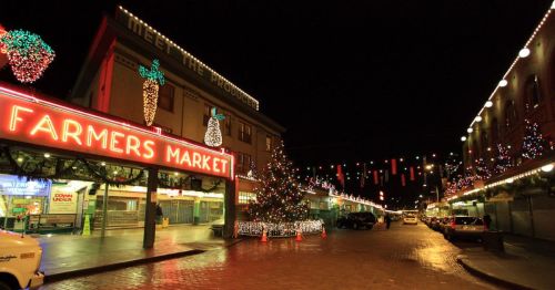 A festive farmers market at night, adorned with colorful lights and a Christmas tree, creating a cheerful holiday atmosphere.