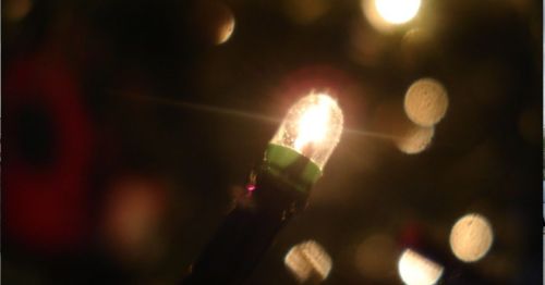 A close-up of a glowing Christmas light bulb with a blurred background of festive lights.