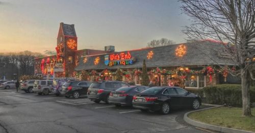 A festive boutique decorated with holiday lights and ornaments, surrounded by parked cars at sunset.