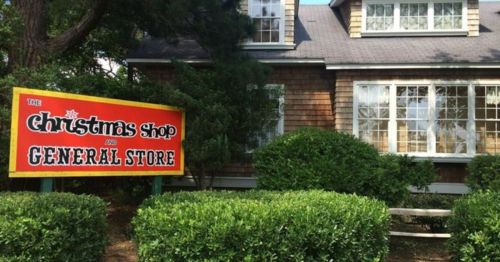 A charming building with a sign reading "The Christmas Shop and General Store" surrounded by greenery.