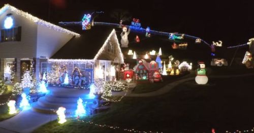 A festive house decorated with colorful Christmas lights, inflatables, and holiday decorations in a nighttime setting.