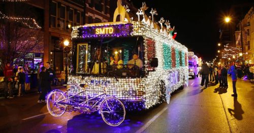 A brightly lit parade float decorated with colorful lights, featuring a bus and a bicycle, during a nighttime event.
