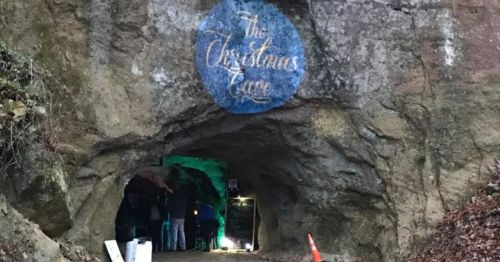 Entrance to a cave with a sign reading "The Christmas Cave," surrounded by rocky terrain and soft lighting.