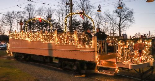 A festive train adorned with lights and decorations, parked in a scenic area during twilight.