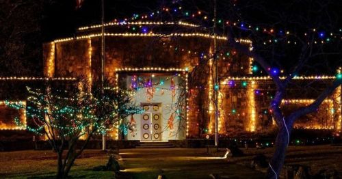 A beautifully lit building adorned with colorful holiday lights at night, surrounded by trees and decorations.