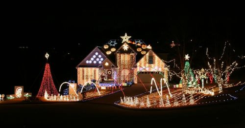 A beautifully decorated house with colorful Christmas lights, featuring trees, stars, and festive displays in a dark setting.