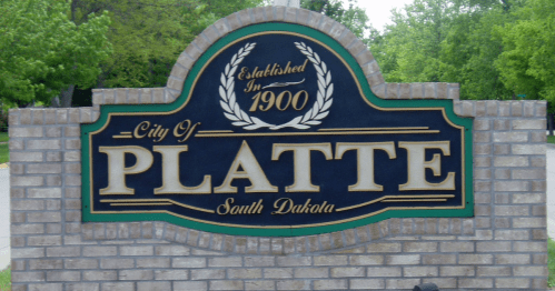 Sign for the city of Platte, South Dakota, established in 1900, featuring decorative elements and a brick background.