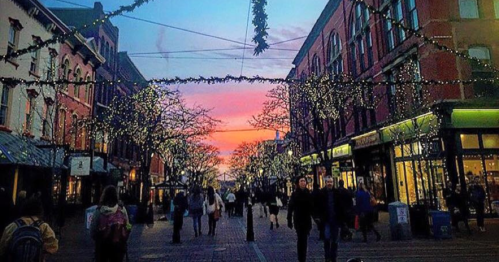 A vibrant street scene at dusk, adorned with festive lights and a colorful sunset in the background.