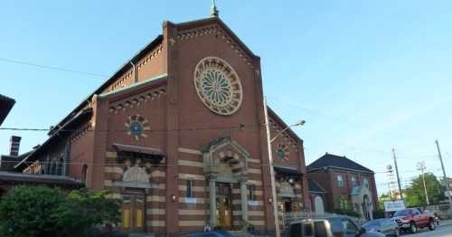 Historic brick building with a large rose window, featuring ornate architectural details and a clear blue sky.