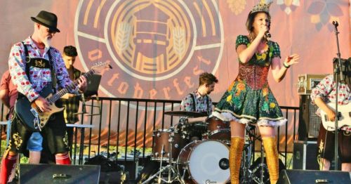 A lively band performs on stage at Oktoberfest, featuring a singer in a colorful dress and musicians in festive attire.