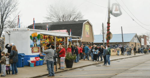 A festive street scene with a food truck, people in line, and holiday decorations on a cloudy day.