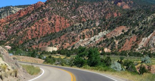 Curving road through a scenic landscape with red and green mountains in the background and lush vegetation.