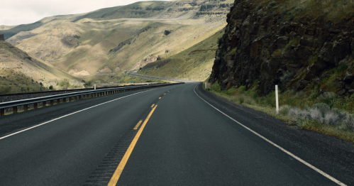 A winding road through a mountainous landscape with dry hills and rocky cliffs on either side.